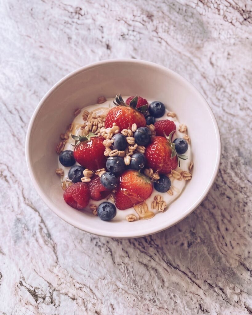 healthy yogurt bowl with fresh strawberries, blueberries, raspberries, granola, and honey on a marble countertop, perfect for a nutritious breakfast.