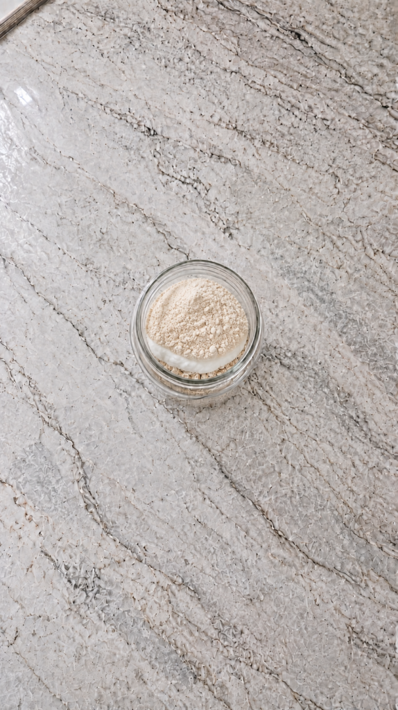 overnight oats being stirred with spoon in glass jar on marble countertop
