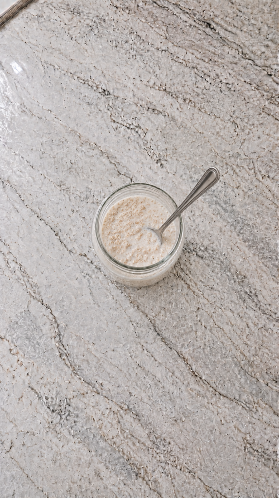 protein powder added to overnight oats mixture in glass jar on marble countertop