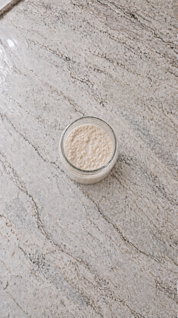 greek yogurt added on top of rolled oats in glass jar on marble countertop