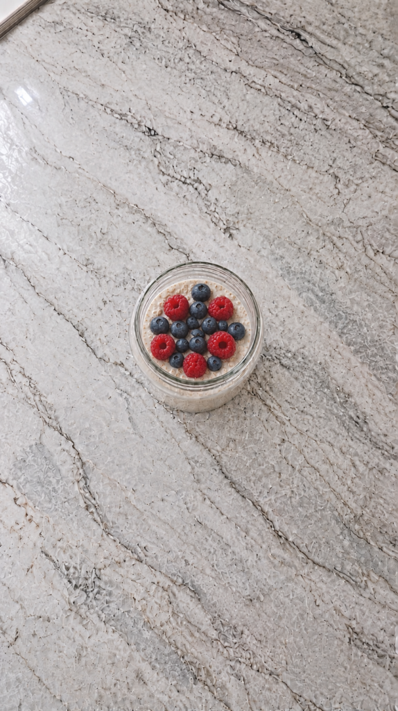 High Protein Overnight Oats For Weight Loss high protein overnight oats in a glass jar topped with raspberries and blueberries on marble countertop