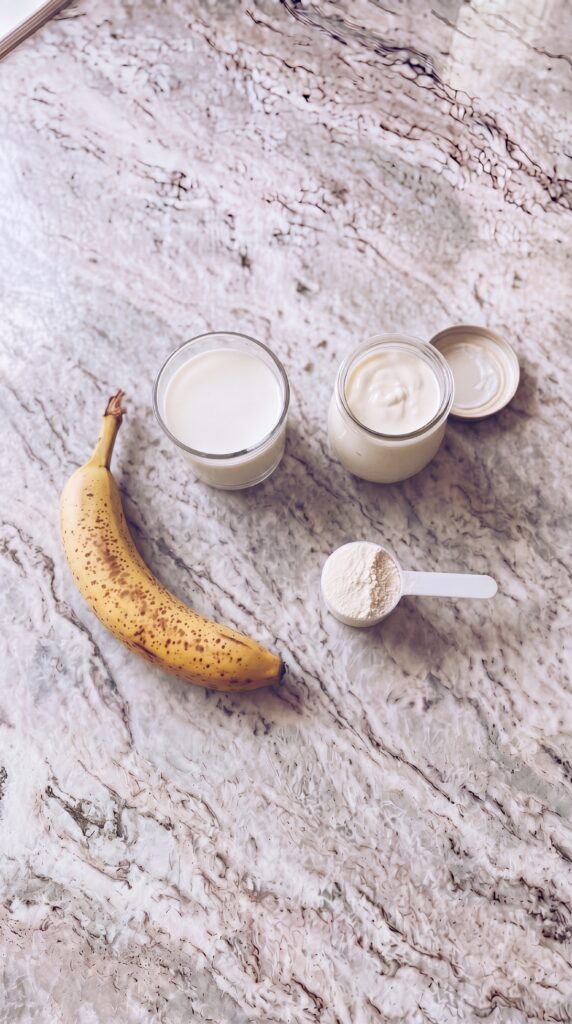 banana greek yogurt protein powder and milk ingredients for high protein smoothie on marble countertop