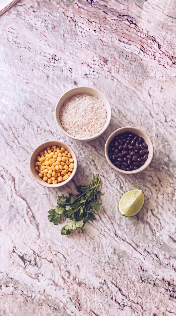 Easy High Protein Burrito Bowls For Meal Prep rice black beans corn cilantro and lime ingredients for high protein burrito bowls on marble countertop