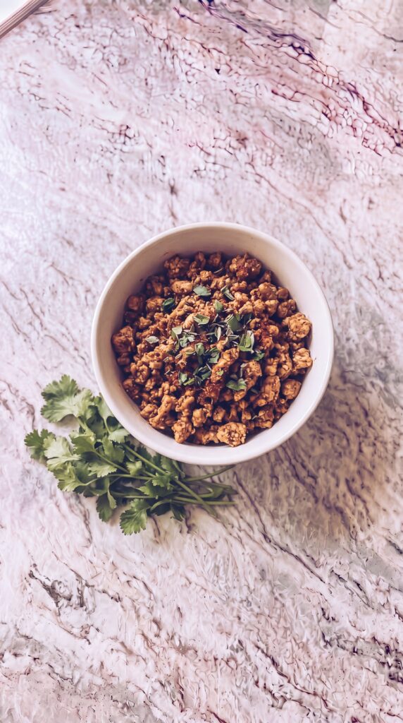 Easy High Protein Burrito Bowls For Meal Prep seasoned cooked ground turkey in a white bowl with cilantro on marble countertop