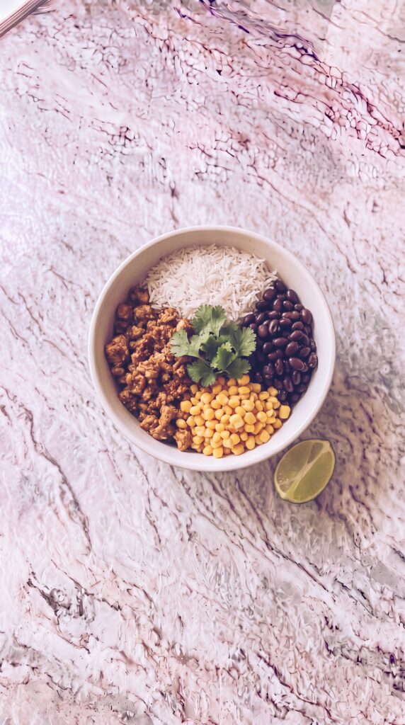 Easy High Protein Burrito Bowls For Meal Prep high protein burrito bowl with rice black beans corn turkey cilantro and lime on marble countertop