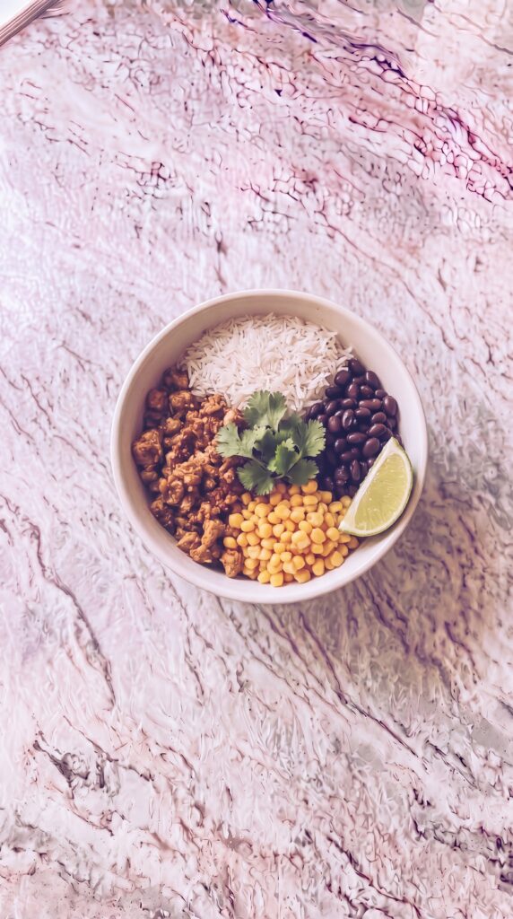 Easy High Protein Burrito Bowls For Meal Prep high protein burrito bowl with rice black beans corn and cilantro with lime wedge on marble countertop