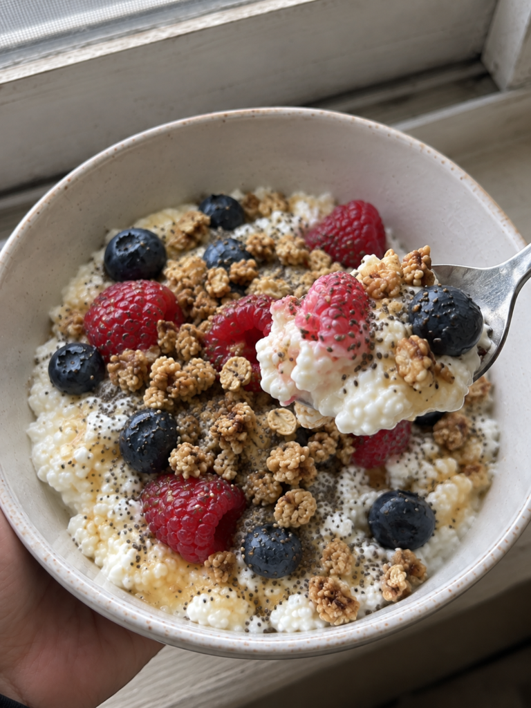 spoon lifting bite of high protein cottage cheese bowl with berries and granola close up